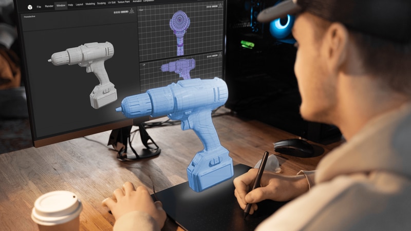 Man working on a 3D model of an electric screwdriver behind a computer screen with 2D blueprints of the screwdriver.