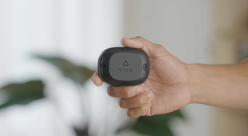 A hand holding up the VIVE Ultimate Tracker to show its compact, rectangular form